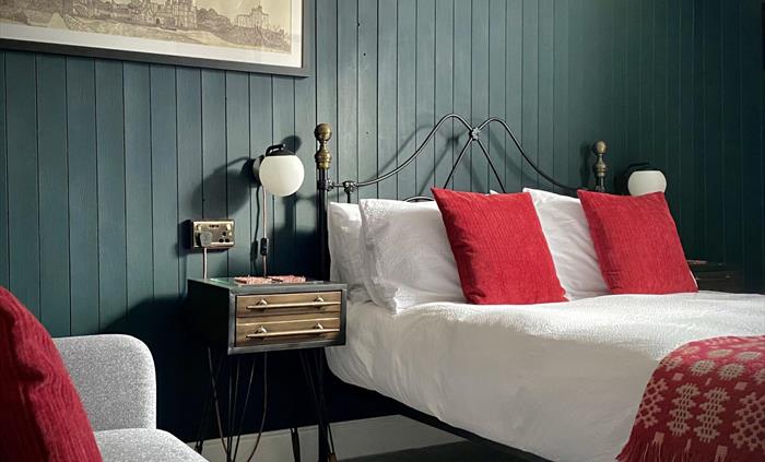 A bedroom at Crafnant House Bed and Breakfast with a bed, white duvet, red cushions and Welsh blanket, against a green panelled wall